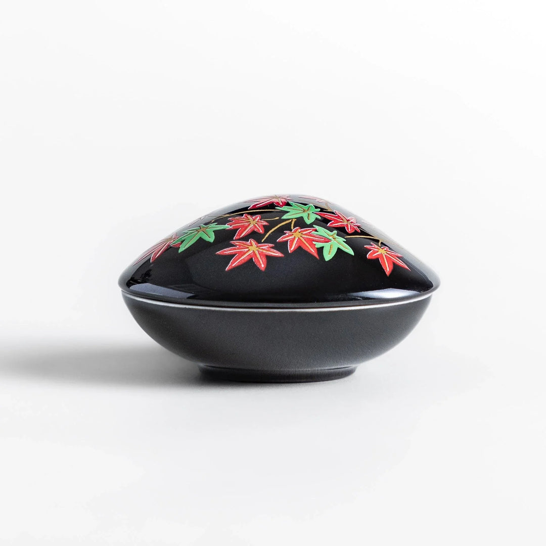 Black seashell-shaped ceramic incense holder with red and green maple leaves and glossy red holder for incense.