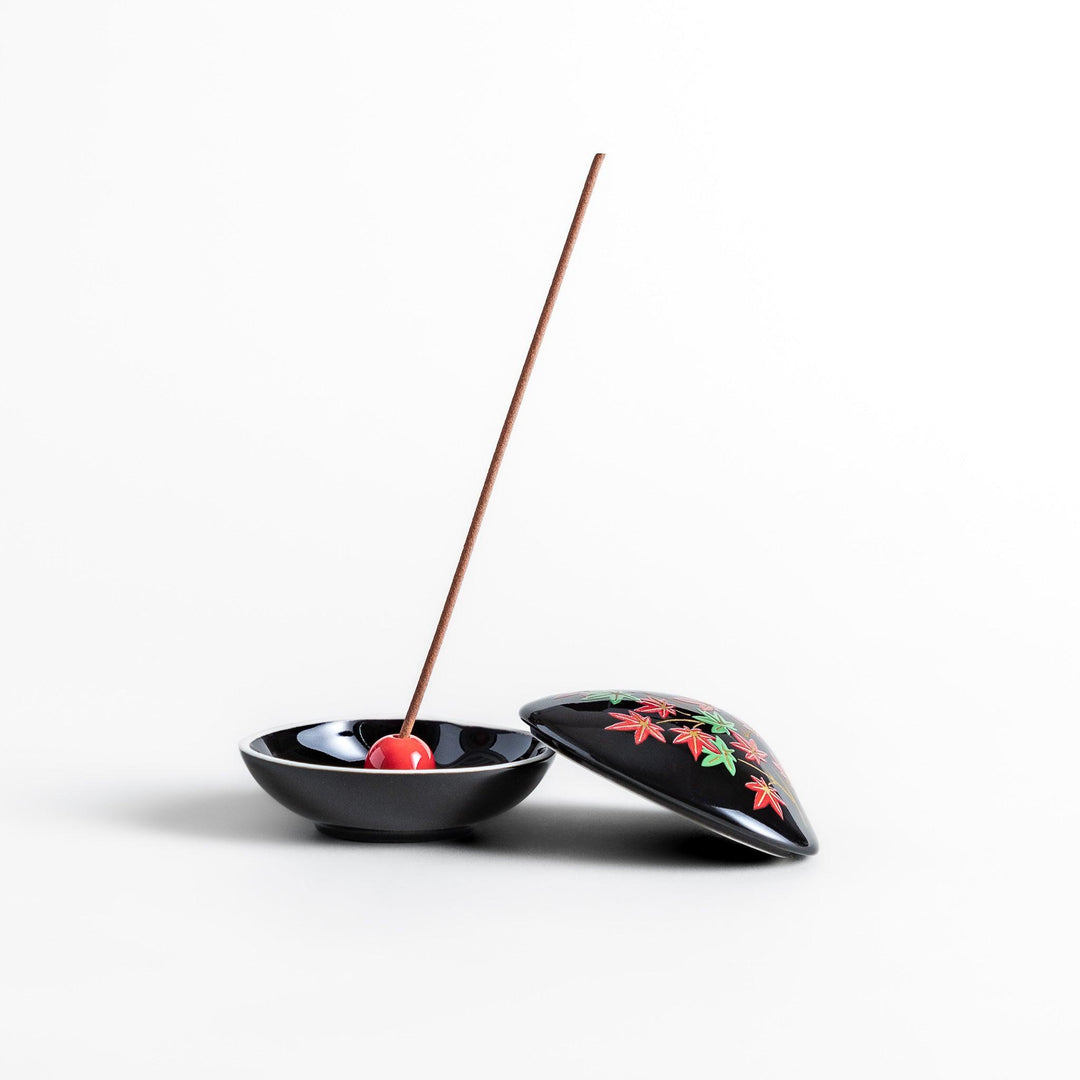 Black seashell-shaped ceramic incense holder with red and green maple leaves and glossy red holder for incense.