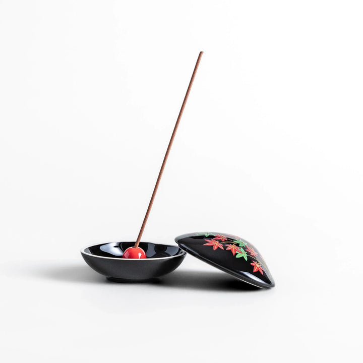 Black seashell-shaped ceramic incense holder with red and green maple leaves and glossy red holder for incense.