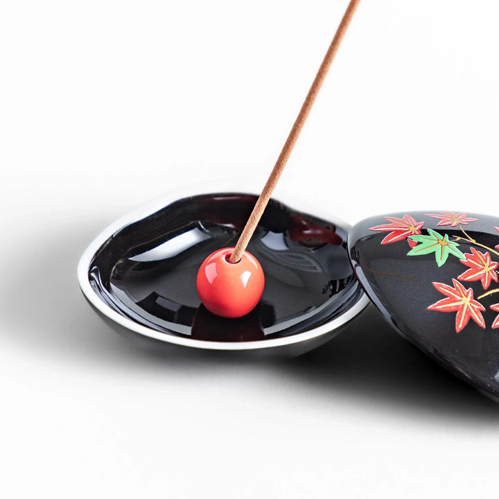 Black seashell-shaped ceramic incense holder with red and green maple leaves and glossy red holder for incense.