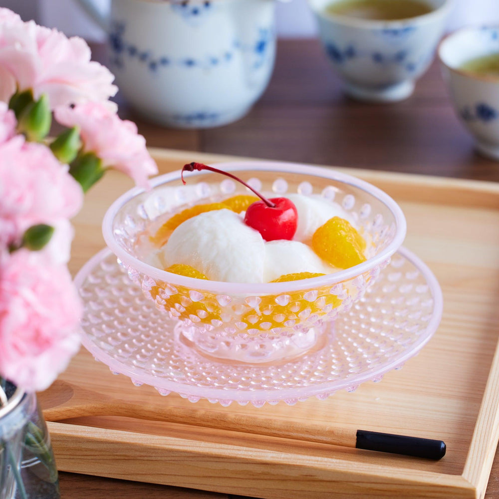 A delicate pink glass dessert bowl with hobnail texture, filled with almond jelly, mandarin slices, and a cherry on top.