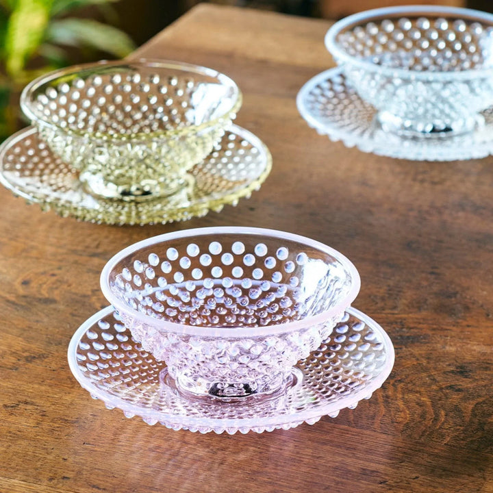 Transparent glass dessert bowl with matching hobnail-patterned saucer on table highlighting raised-dot texture.