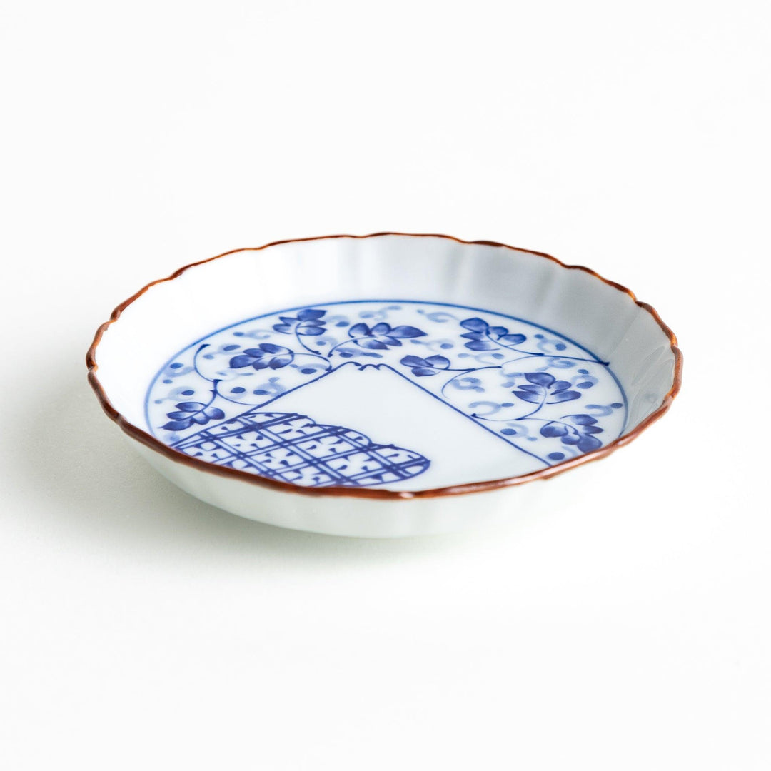 A ceramic dish with a blue and white design, showcasing a pattern of floral motifs and a depiction of Mount Fuji.