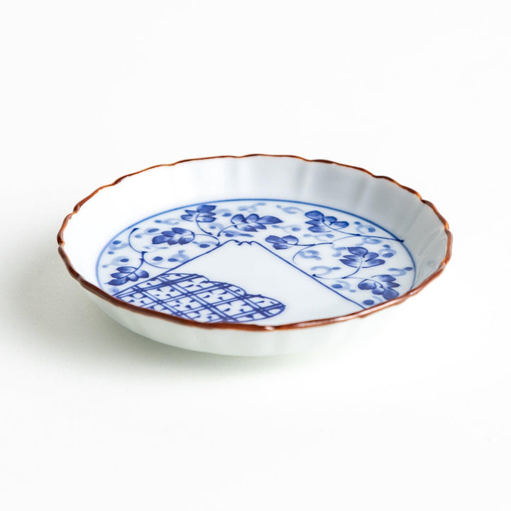 A ceramic dish with a blue and white design, showcasing a pattern of floral motifs and a depiction of Mount Fuji.