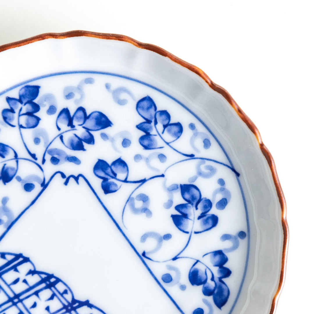 A ceramic dish with a blue and white design, showcasing a pattern of floral motifs and a depiction of Mount Fuji.