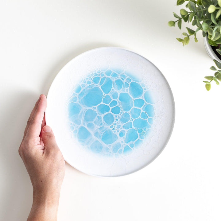 A white salad plate featuring a unique bubble design in shades of blue, resembling frothy ocean waves.