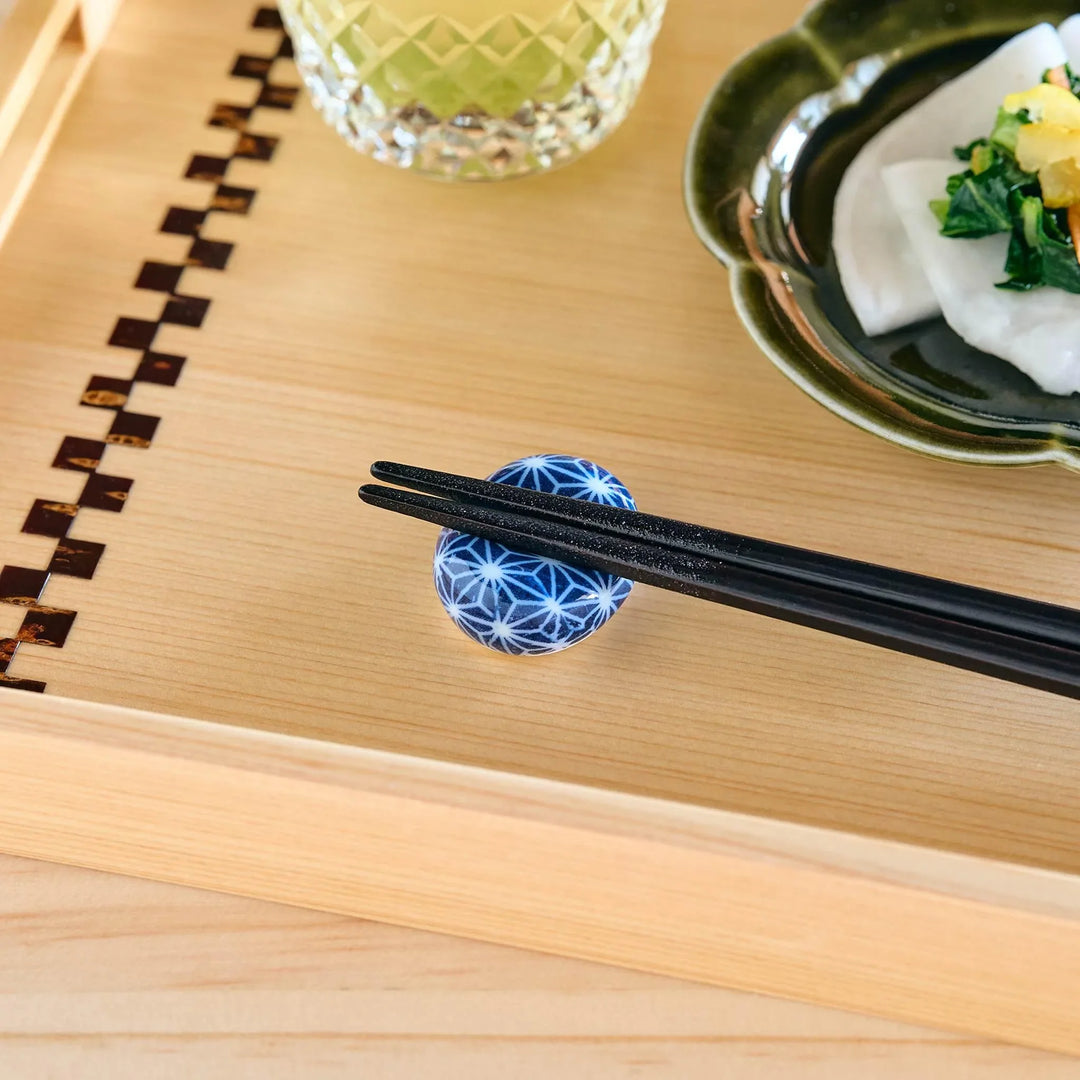 A blue and white hemp leaves patterned chopstick rest shaped like a small ball, holding black chopsticks.