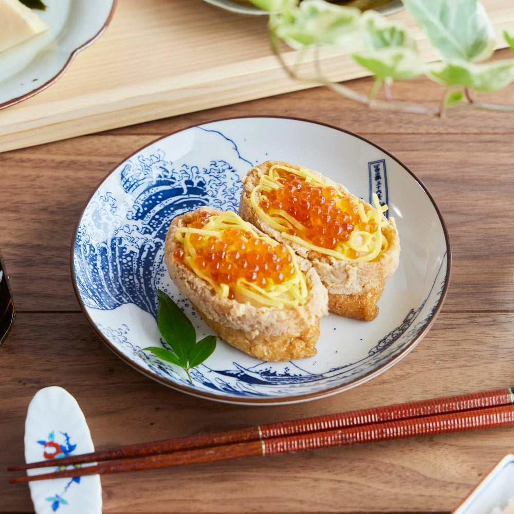 Dessert plate with Hokusai style blue wave design holding two inari sushi with egg and salmon roe topping.