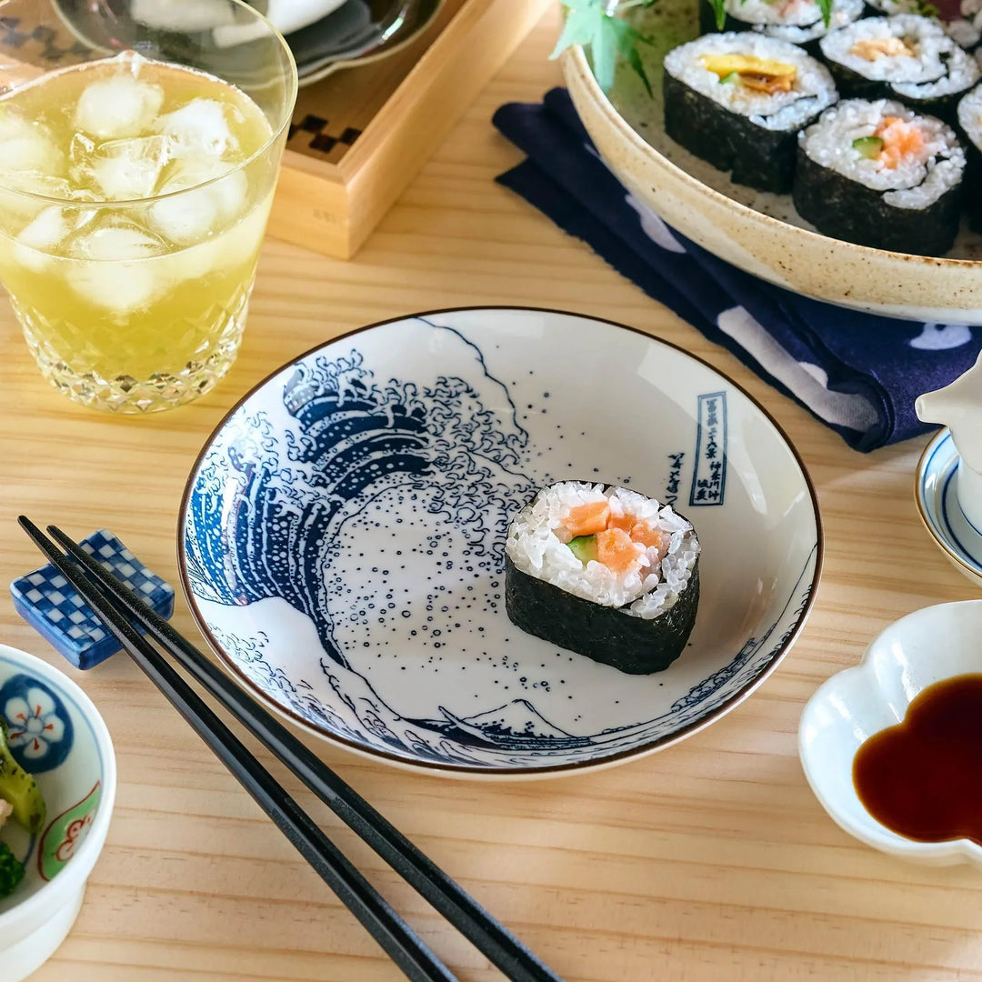 A plate featuring Hokusai’s Great Wave design, with a single sushi roll placed in the center, on a wooden table.