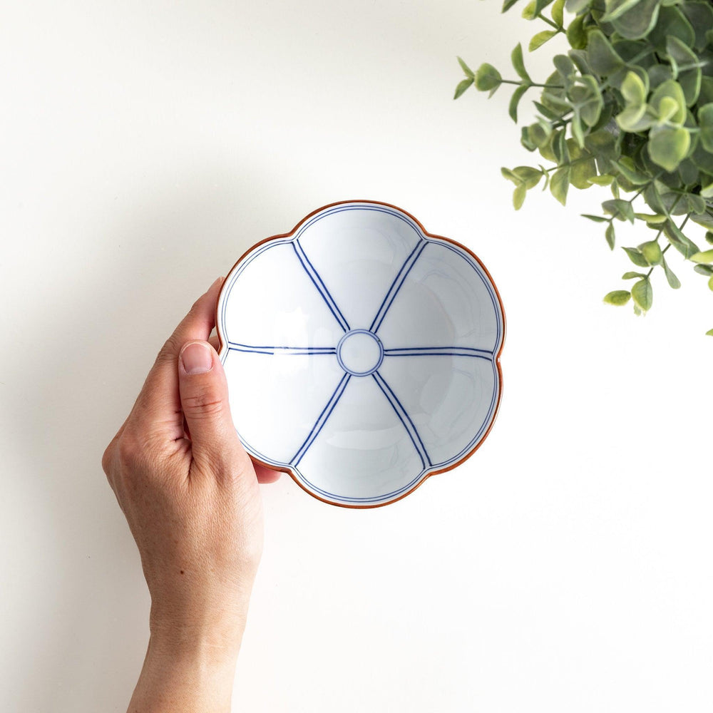 A white ceramic bowl with a floral shape, featuring delicate blue lines and an orange rim.