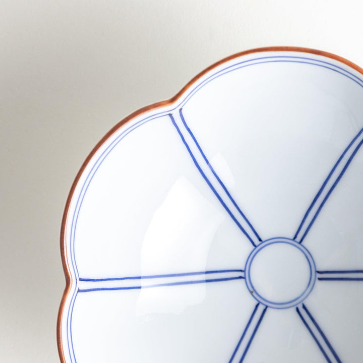 A white ceramic bowl with a floral shape, featuring delicate blue lines and an orange rim.