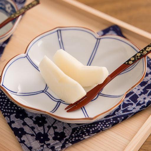Blue lined Japanese dessert plate with pear slices and spoon on patterned cloth atop wooden serving tray.