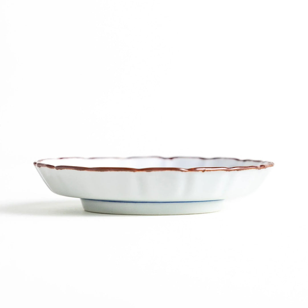 Side view of the porcelain sauce dish, highlighting its low pedestal base and delicate brown-edged raised rim.