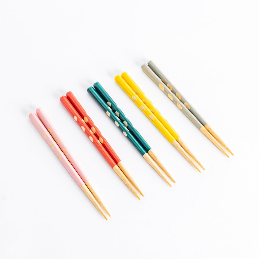 Children’s chopsticks in pink red green yellow and gray with dot patterns and wooden tips for easy grip.