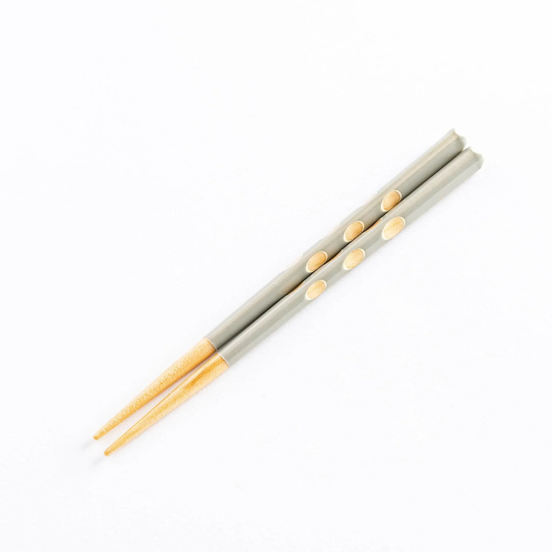 A pair of gray children's chopsticks with light wooden tips and decorative polka dots.