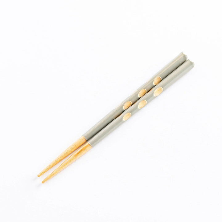 A pair of gray children's chopsticks with light wooden tips and decorative polka dots.