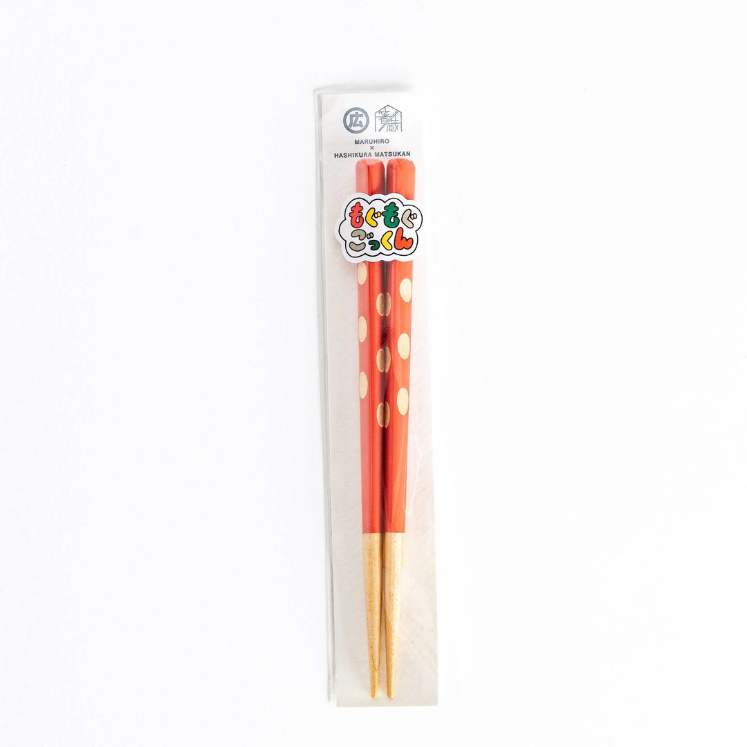  Red children’s chopsticks with beige dots, packaged in clear plastic, displaying the brand logo.