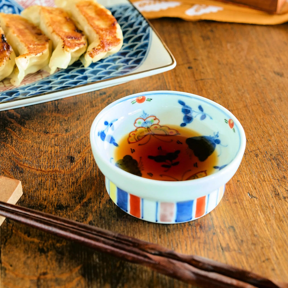 Petite raised Japanese sauce dish with colorful butterflies and floral designs and multicolored striped base.