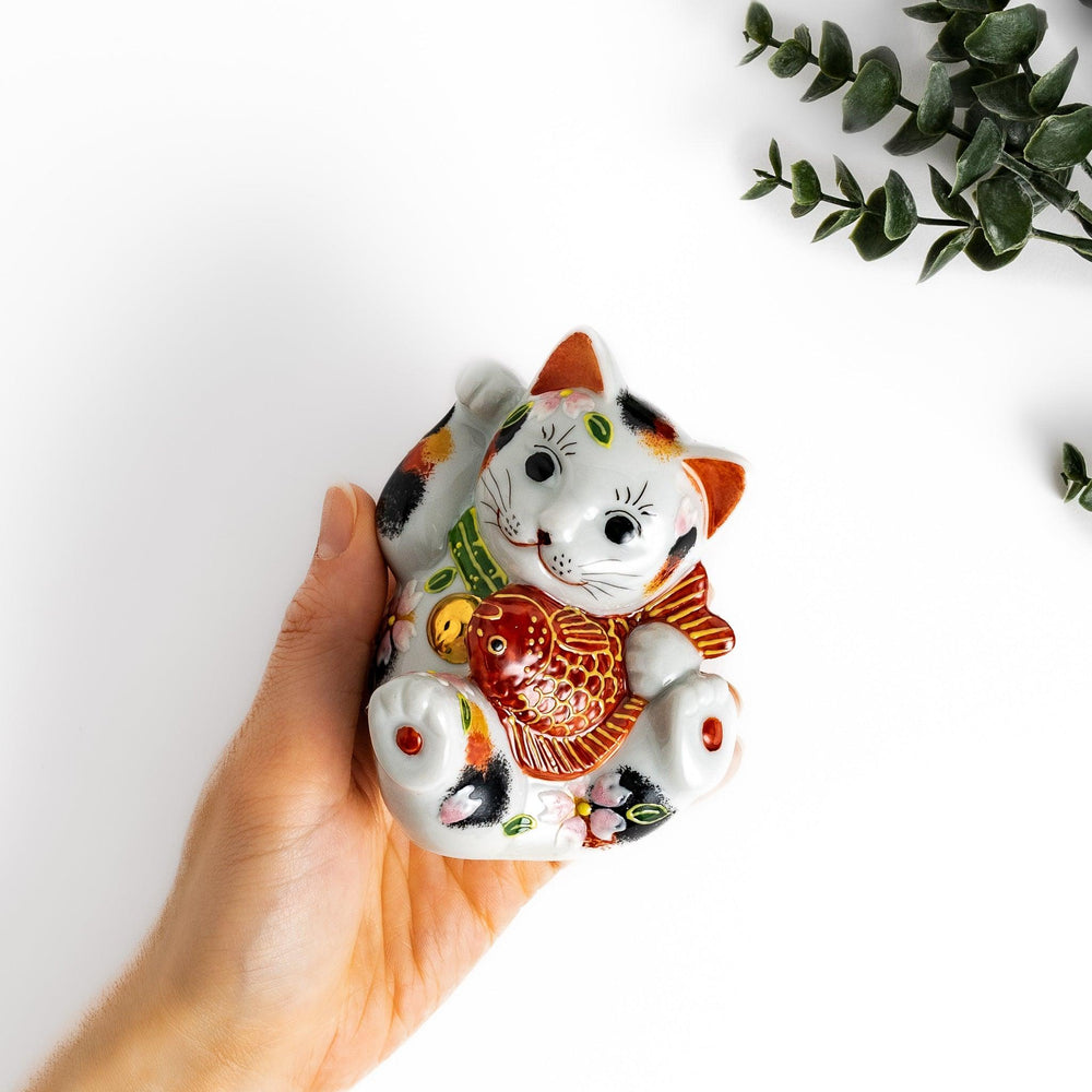 Calico Maneki Neko holding lucky sea bream with floral and leaf patterns symbolizing fortune and prosperity.