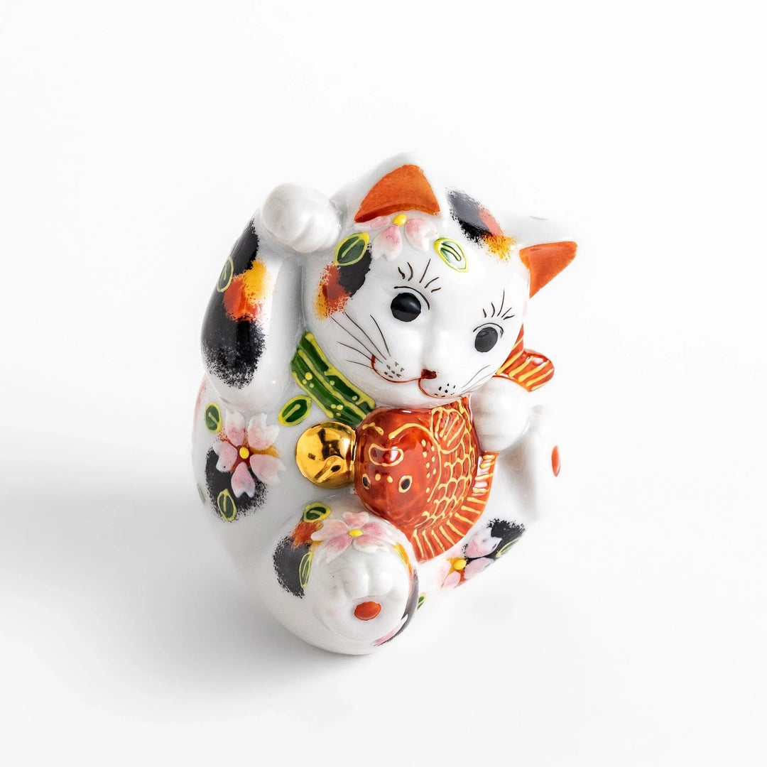 Calico Maneki Neko holding lucky sea bream with floral and leaf patterns symbolizing fortune and prosperity.
