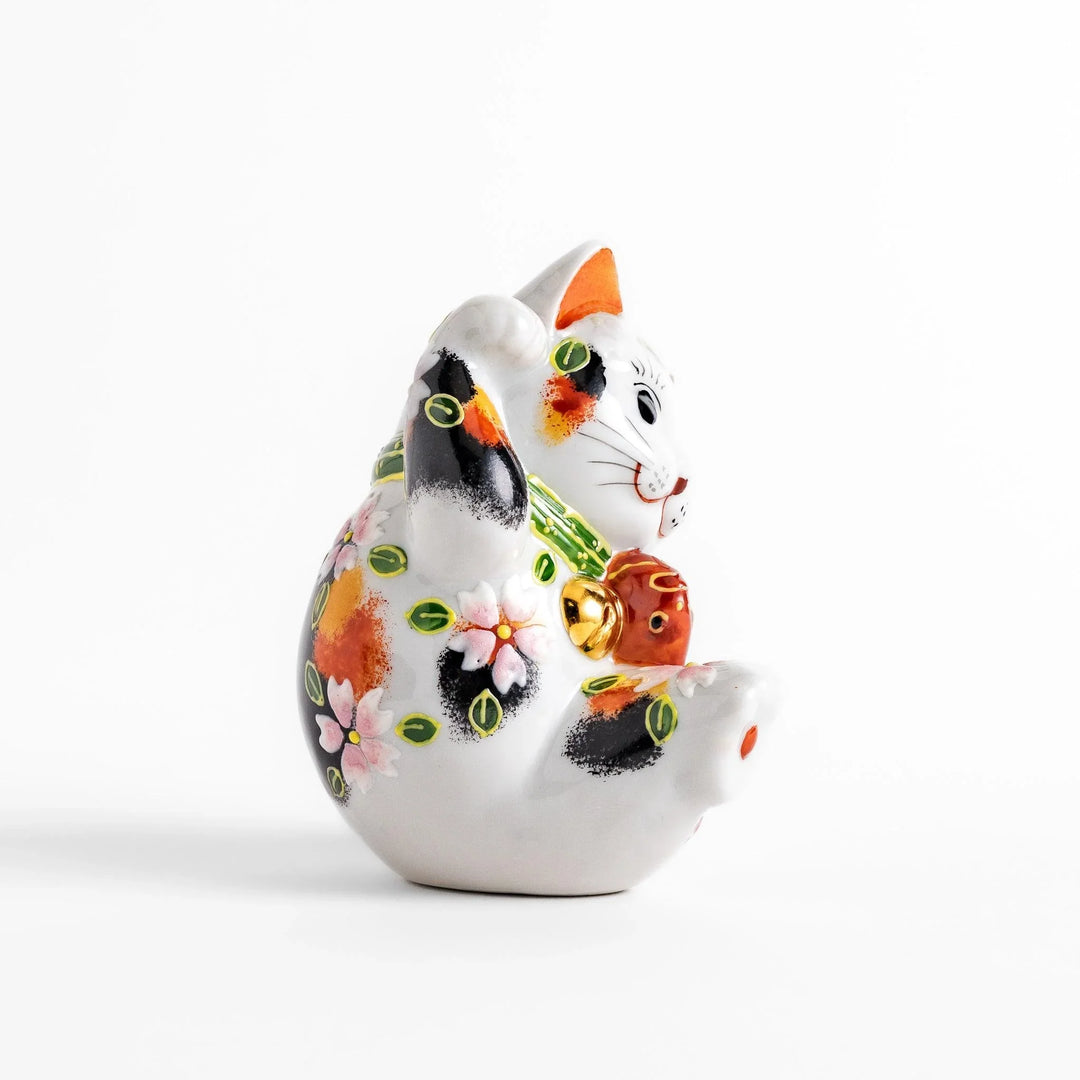 Calico Maneki Neko holding lucky sea bream with floral and leaf patterns symbolizing fortune and prosperity.