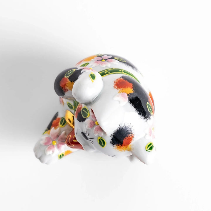 Calico Maneki Neko holding lucky sea bream with floral and leaf patterns symbolizing fortune and prosperity.
