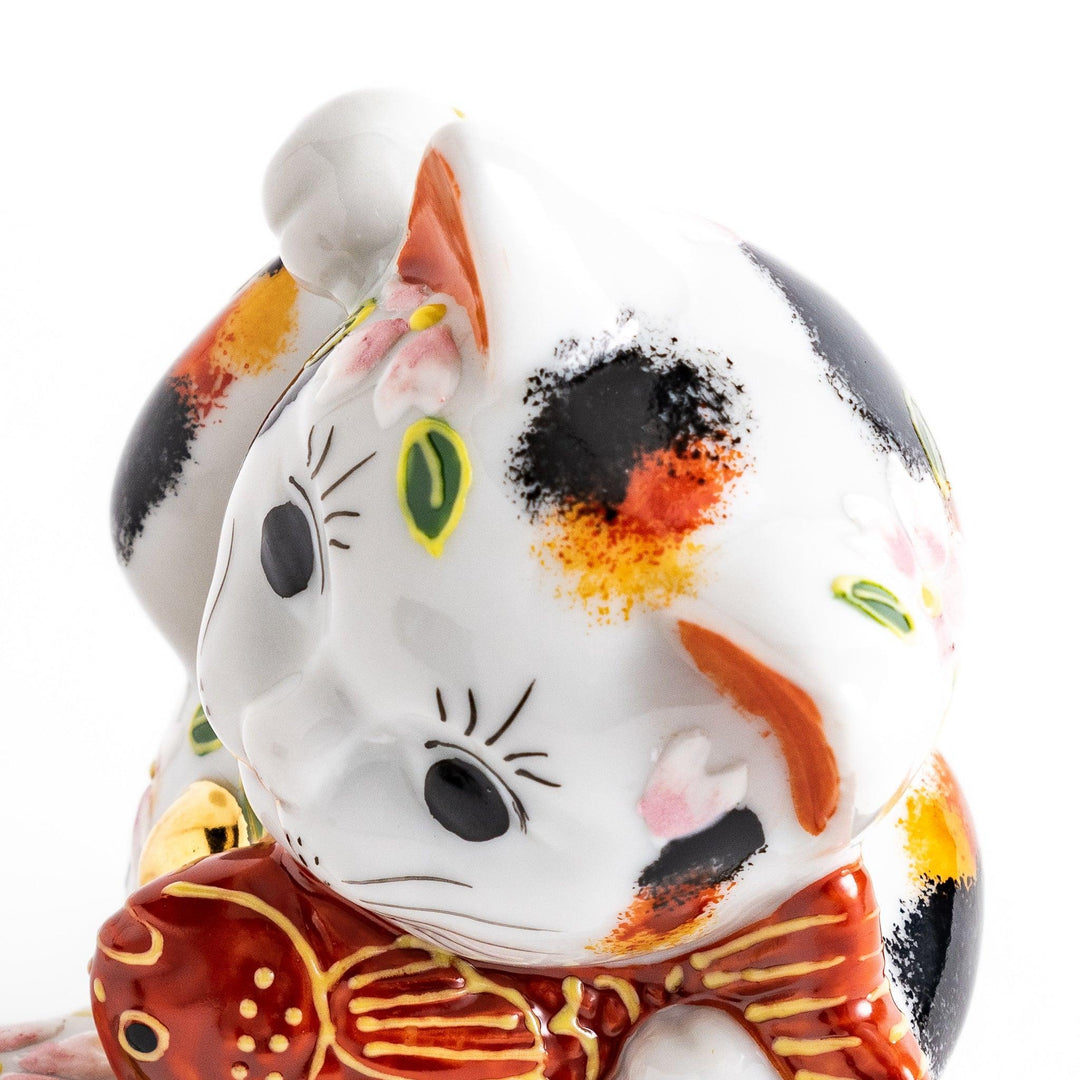 Calico Maneki Neko holding lucky sea bream with floral and leaf patterns symbolizing fortune and prosperity.
