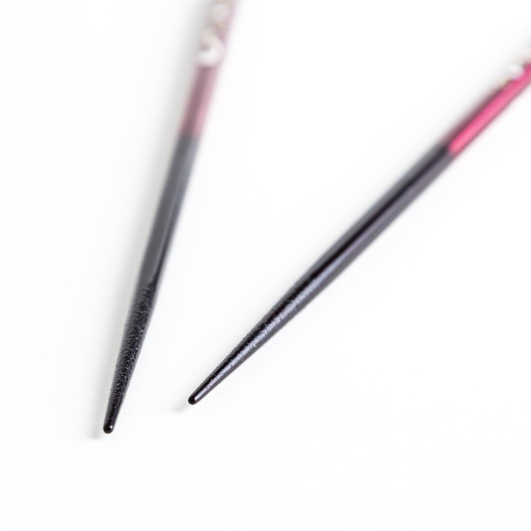 A pair of chopsticks, one blue and one red, each featuring a delicate white cat design near the top.