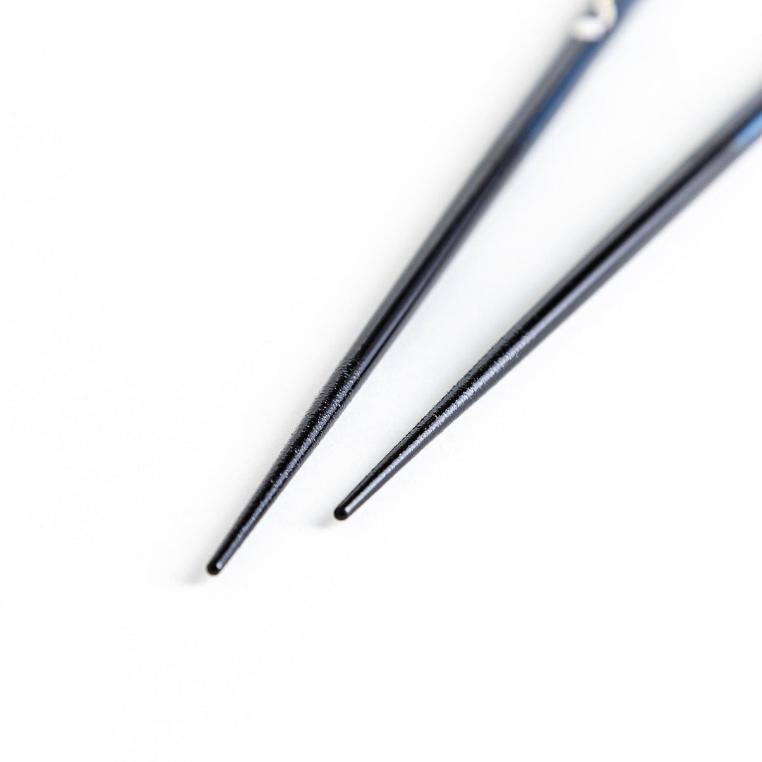 A pair of chopsticks, one blue and one red, each featuring a delicate white cat design near the top.