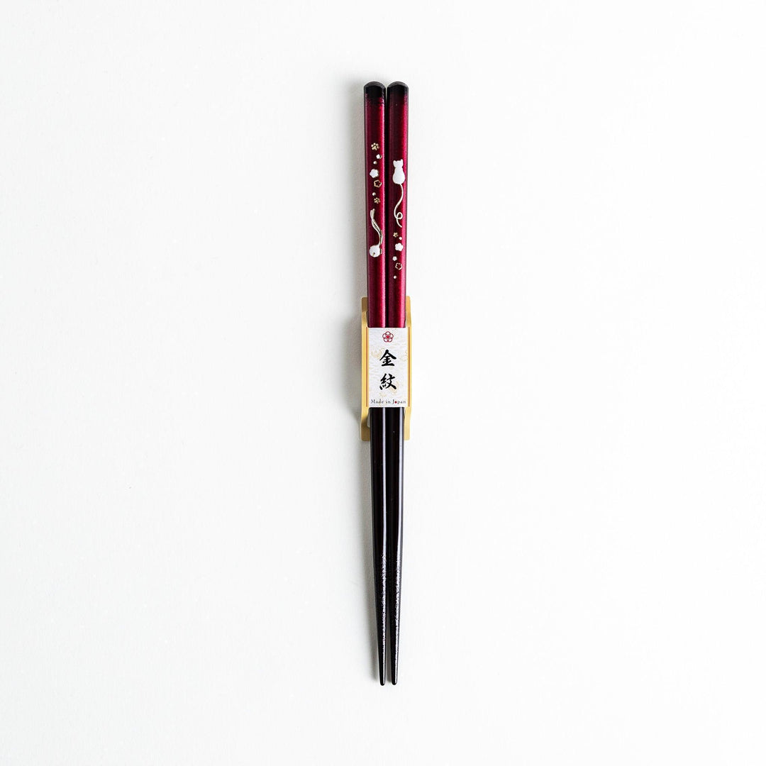 A pair of chopsticks, one blue and one red, each featuring a delicate white cat design near the top.