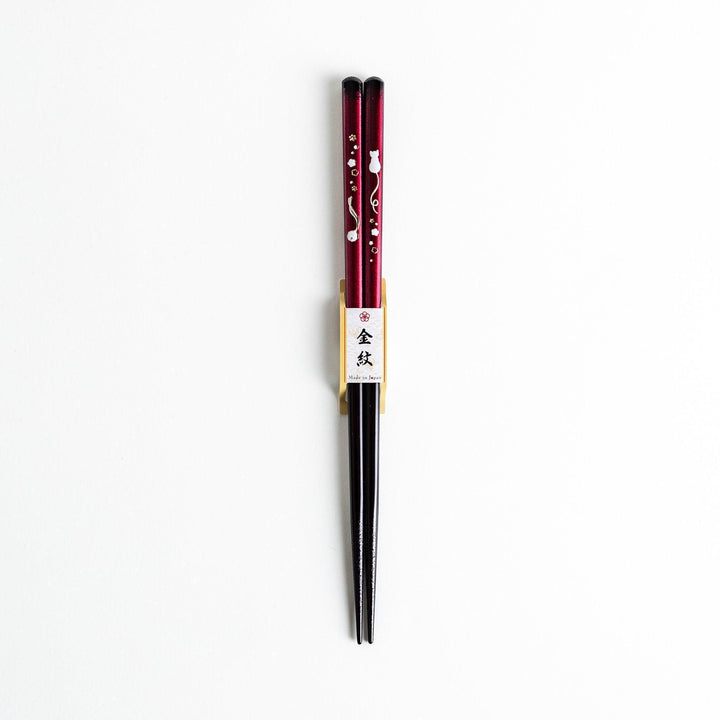 A pair of chopsticks, one blue and one red, each featuring a delicate white cat design near the top.