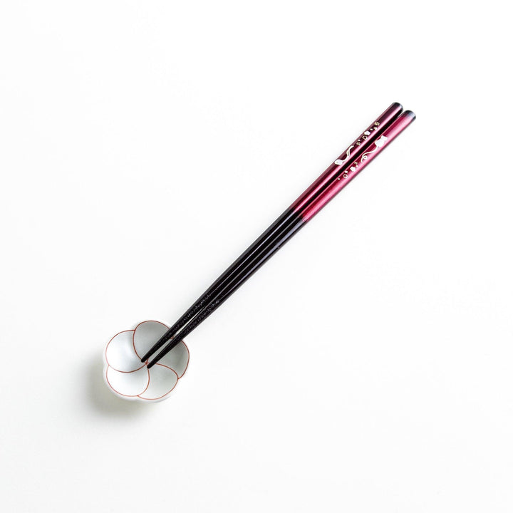A pair of chopsticks, one blue and one red, each featuring a delicate white cat design near the top.