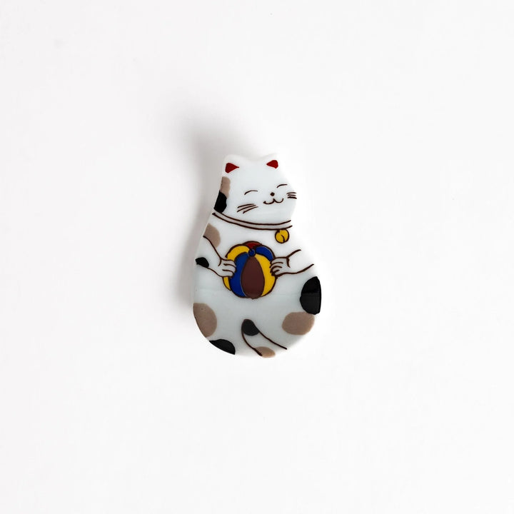 Japanese ceramic cat chopstick rest holding chopsticks with ball motif and colorful detailed design.