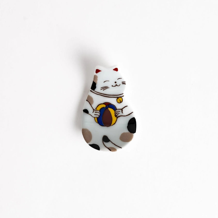 Japanese ceramic cat chopstick rest holding chopsticks with ball motif and colorful detailed design.