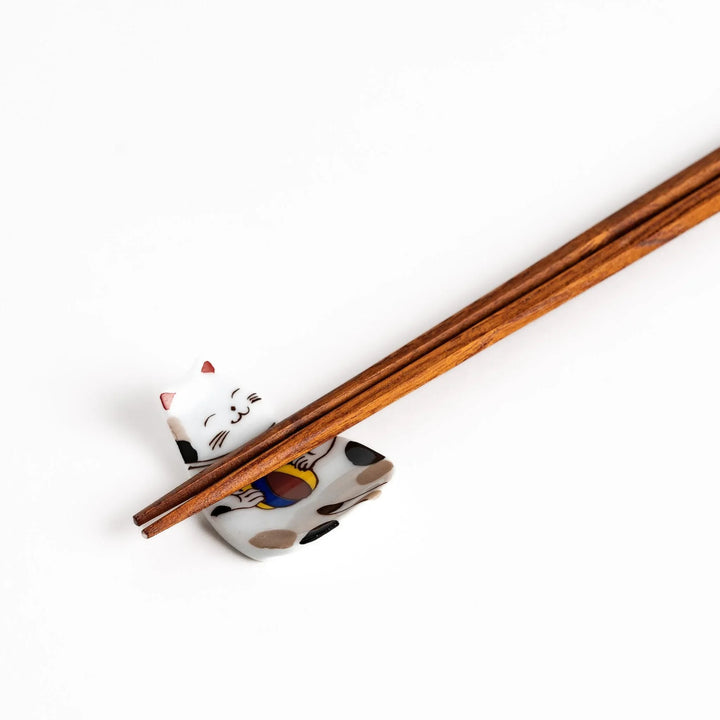 Japanese ceramic cat chopstick rest holding chopsticks with ball motif and colorful detailed design.