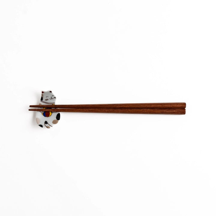 Japanese ceramic cat chopstick rest holding chopsticks with ball motif and colorful detailed design.