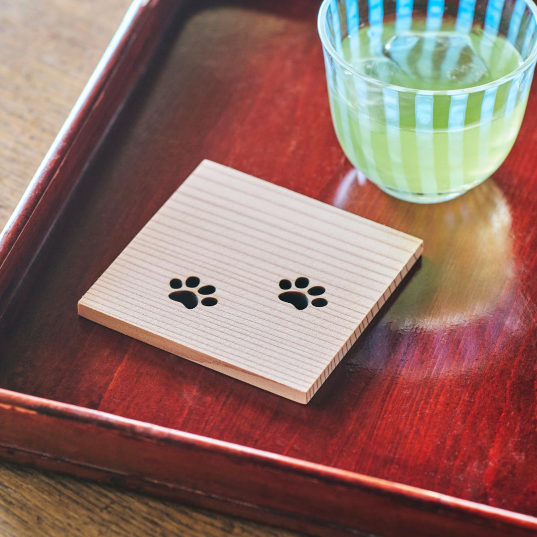 Natural Japanese cedar wood coaster featuring cat paw designs placed on a red lacquer tray for traditional dining