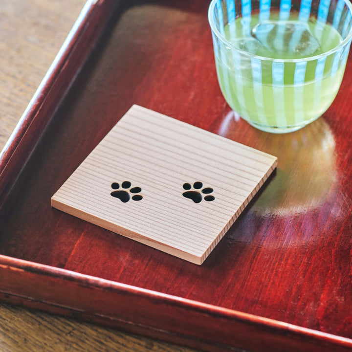 Natural Japanese cedar wood coaster featuring cat paw designs placed on a red lacquer tray for traditional dining