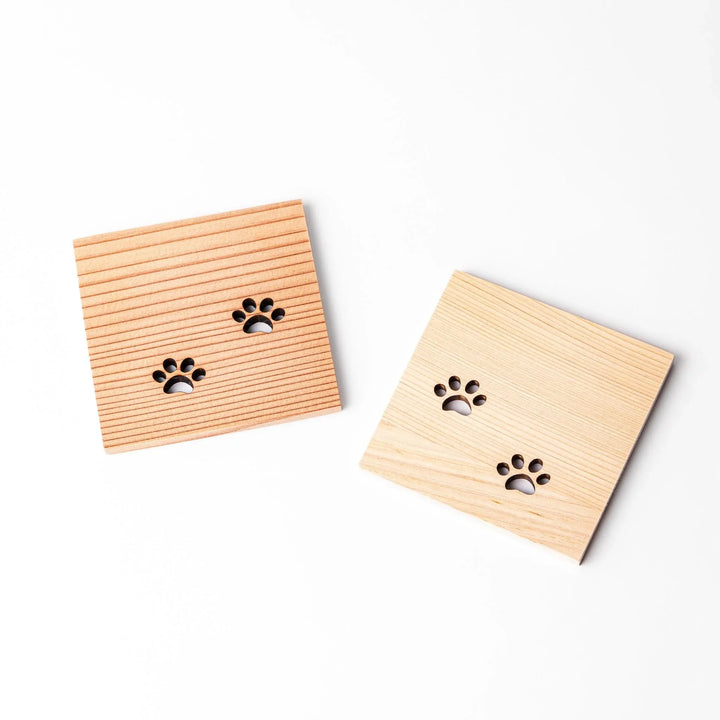 Two square wooden mini coasters featuring cat paw cutouts, showcasing hinoki and cedar tones in angled arrangement