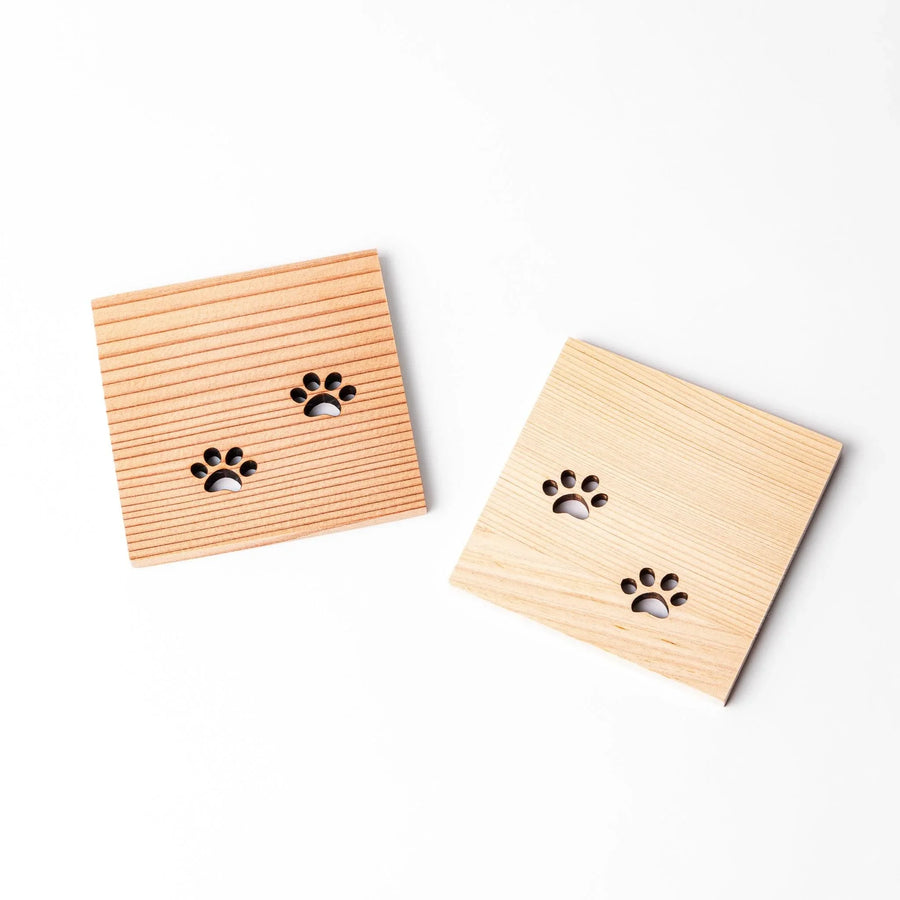 Two square wooden mini coasters featuring cat paw cutouts, showcasing hinoki and cedar tones in angled arrangement