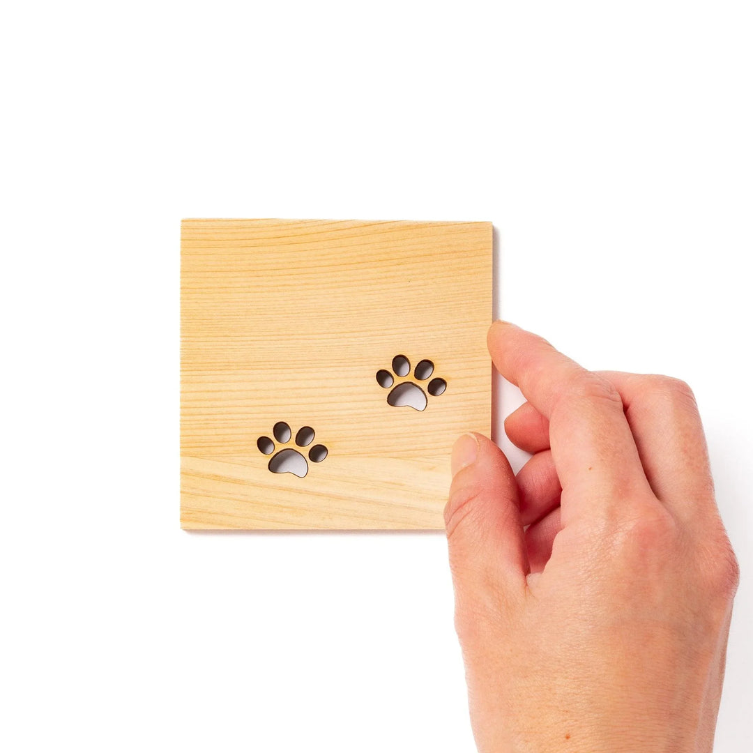 Square hinoki wood mini coaster with two cat paw cutouts, showcasing light grain and protecting surfaces.