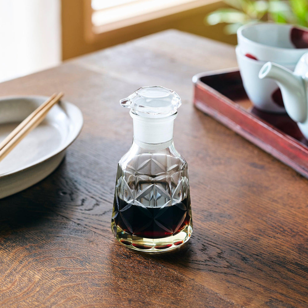 A patterned glass soy sauce dispenser filled with dark soy sauce, adding elegance to a Japanese dining setting.