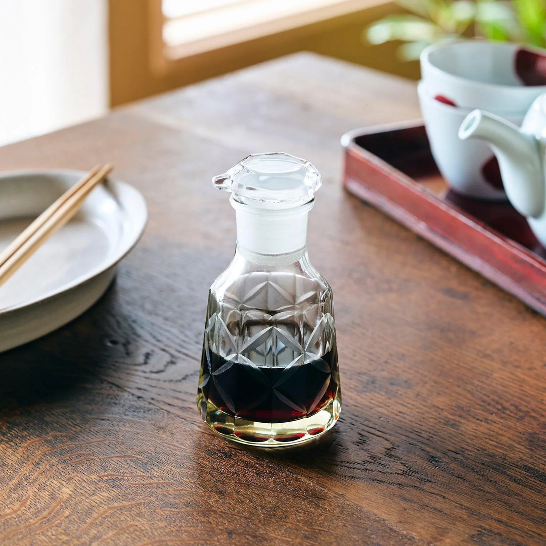 A patterned glass soy sauce dispenser filled with dark soy sauce, adding elegance to a Japanese dining setting.