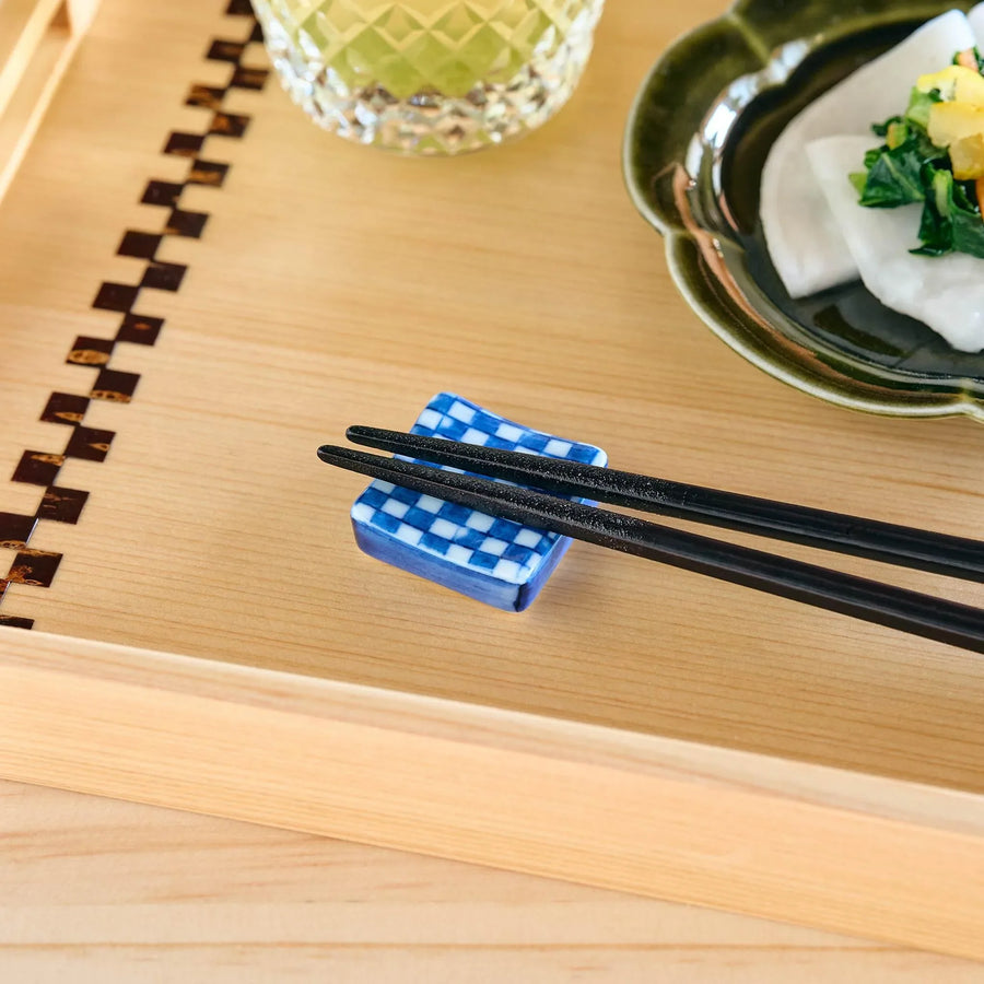 A blue and white checkered square chopstick rest supporting black chopsticks.