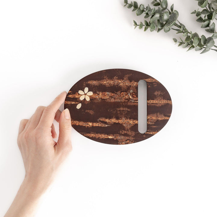 Oval-shaped cherry bark teapot rest with a beautiful natural grain and a delicate cherry blossom inlay, adding a touch of elegance to your tea time.