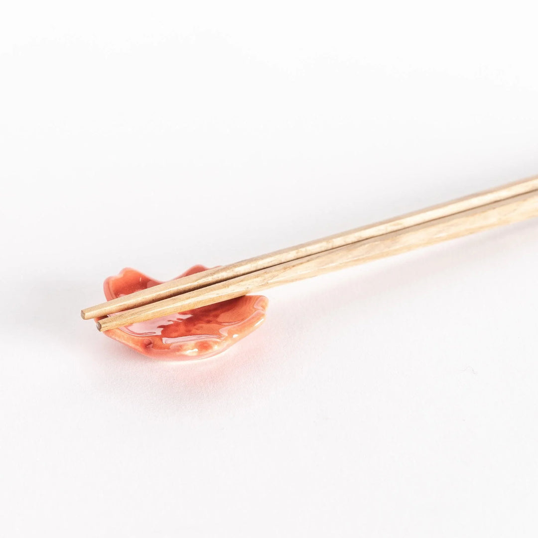 Close-up of a vermilion cherry blossom chopstick rest with chopsticks resting gently across its glossy surface.
