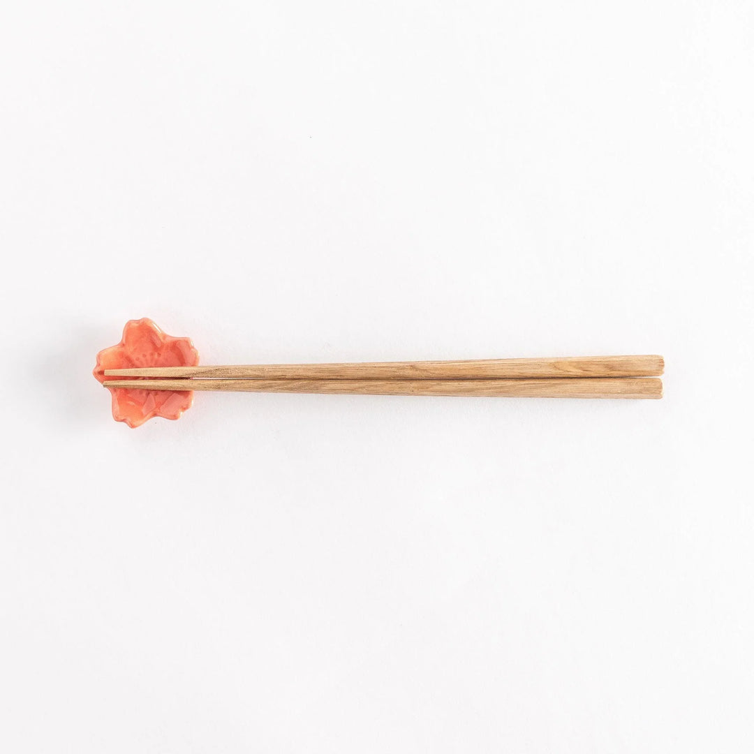 Vermilion cherry blossom chopstick rest holding chopsticks, highlighting its glossy finish and floral design.