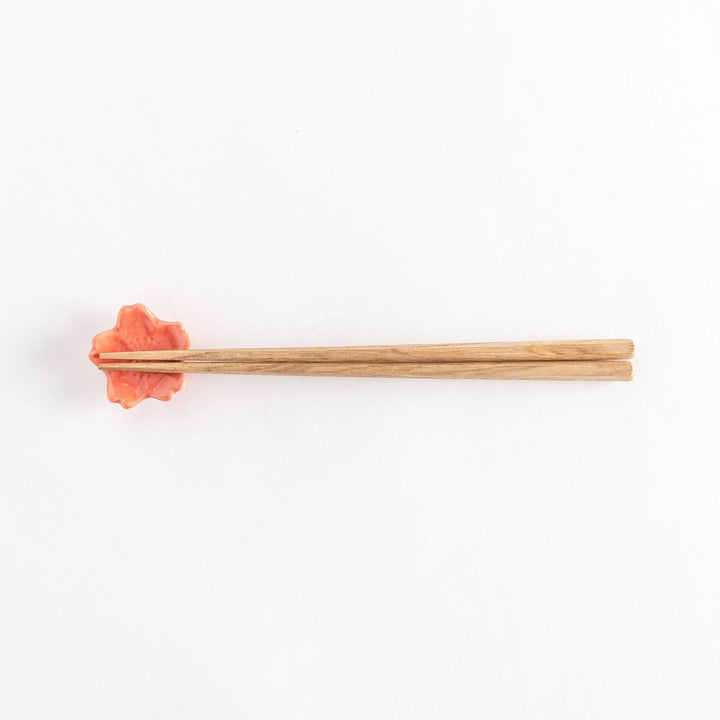 Vermilion cherry blossom chopstick rest holding chopsticks, highlighting its glossy finish and floral design.