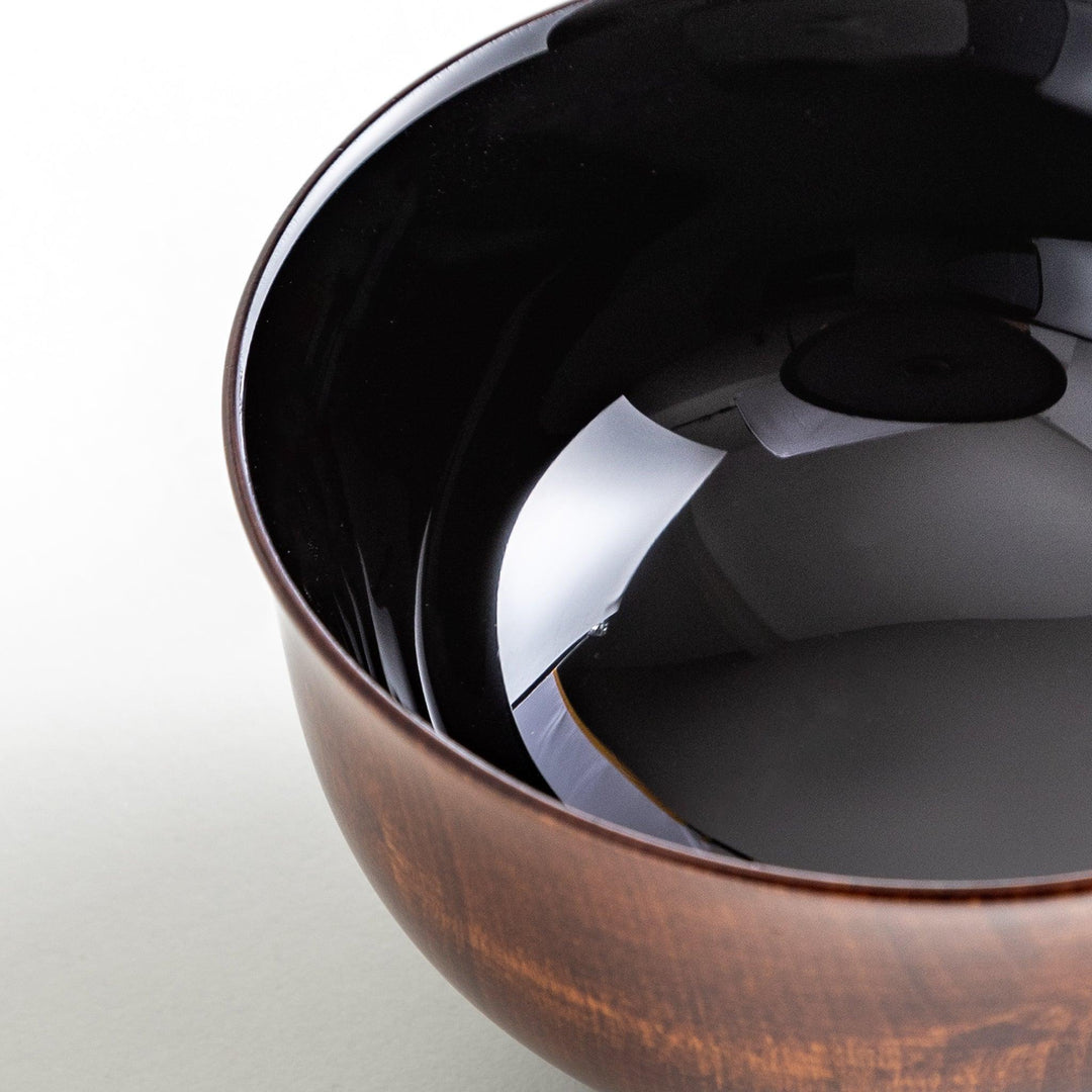 A wooden soup bowl featuring a dark brown grain finish with a sleek black interior.
