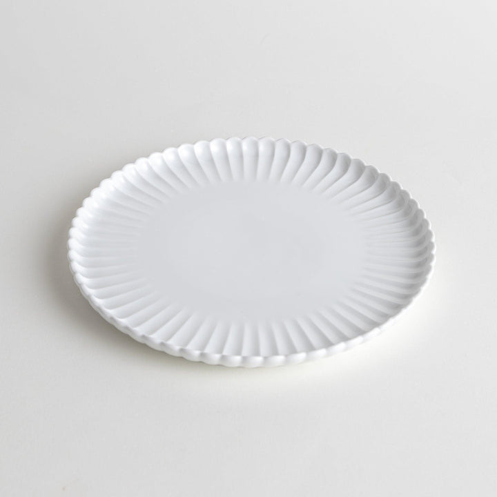 A white ceramic salad plate with a scalloped design with raised edges.
